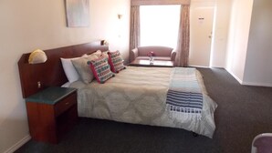 A hotel room with a large bed, a nightstand, a desk, a chair, and a window with curtains. - Yass Motel (Yass)