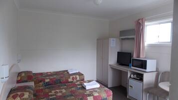 A hotel room with two beds, a desk with a computer and microwave, a chair, and a window with curtains.