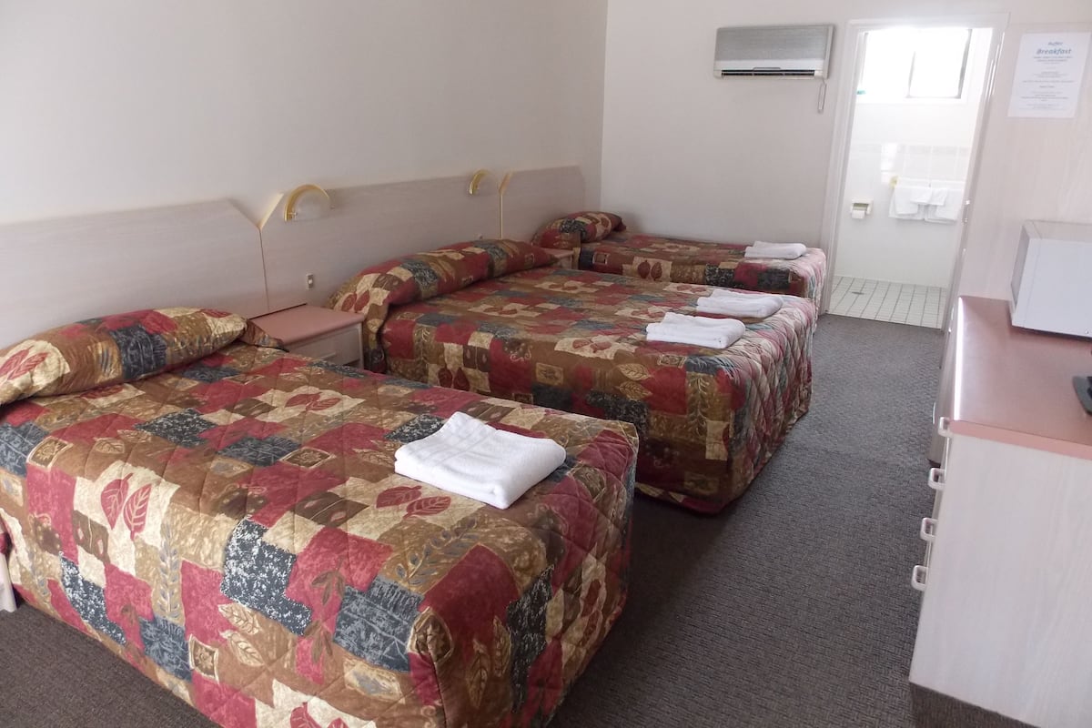 Habitación de hotel con tres camas, cada una con colcha estampada, un escritorio con silla y un equipo de aire acondicionado en la pared.