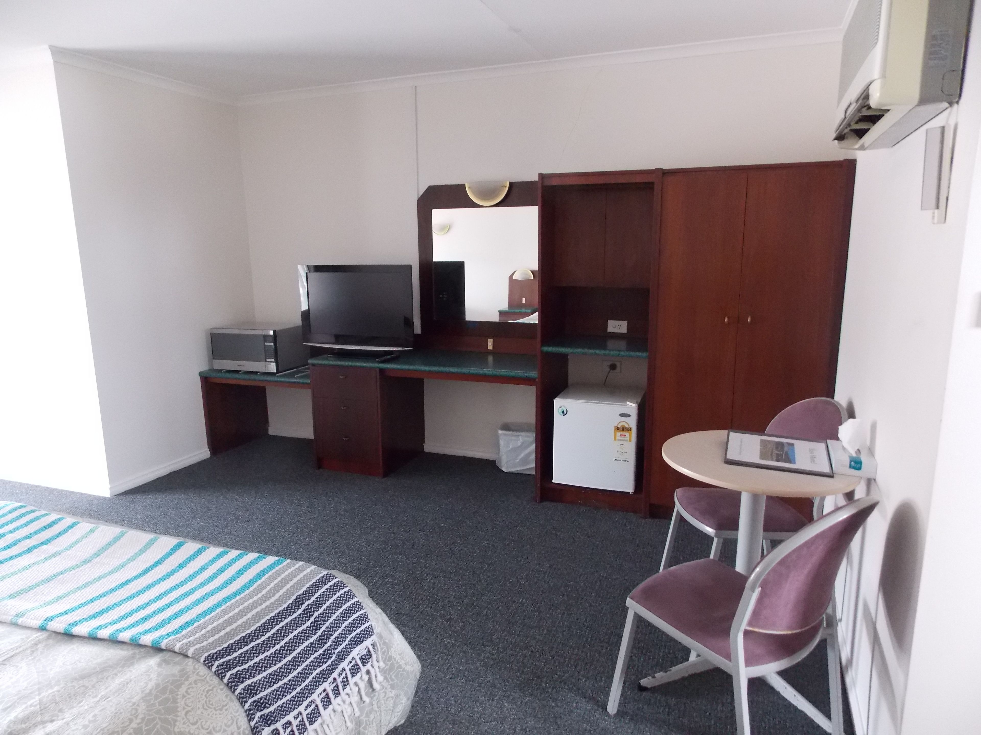 A hotel room with a bed, a desk with a computer, a television, a small refrigerator, and a chair.