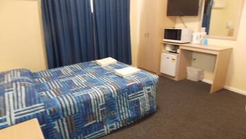 Ein Hotelzimmer mit einem Bett, einem Schreibtisch mit Computer, einer Mikrowelle und einem kleinen Kühlschrank.