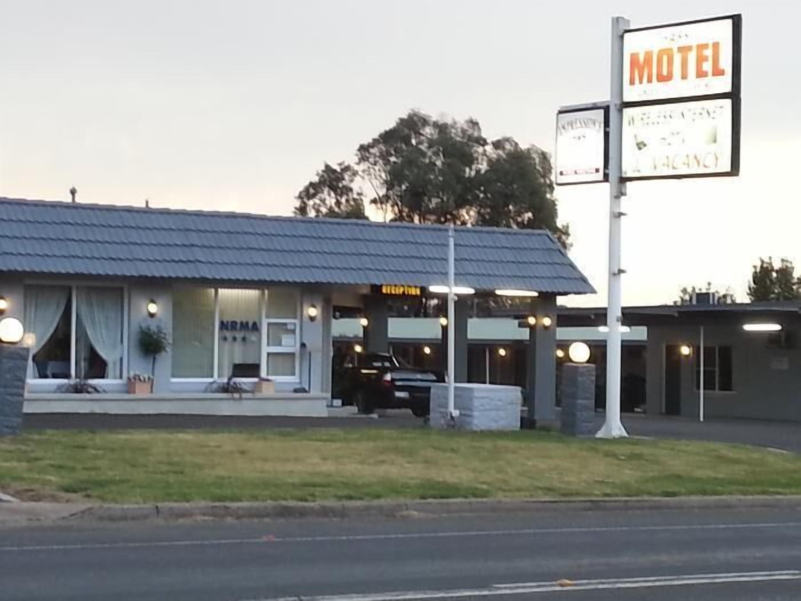 Un motel con estructura de una sola planta, un área de estacionamiento visible y un letrero que indica la disponibilidad.