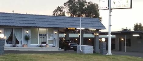 Un motel con estructura de una sola planta, un área de estacionamiento visible y un letrero que indica la disponibilidad.