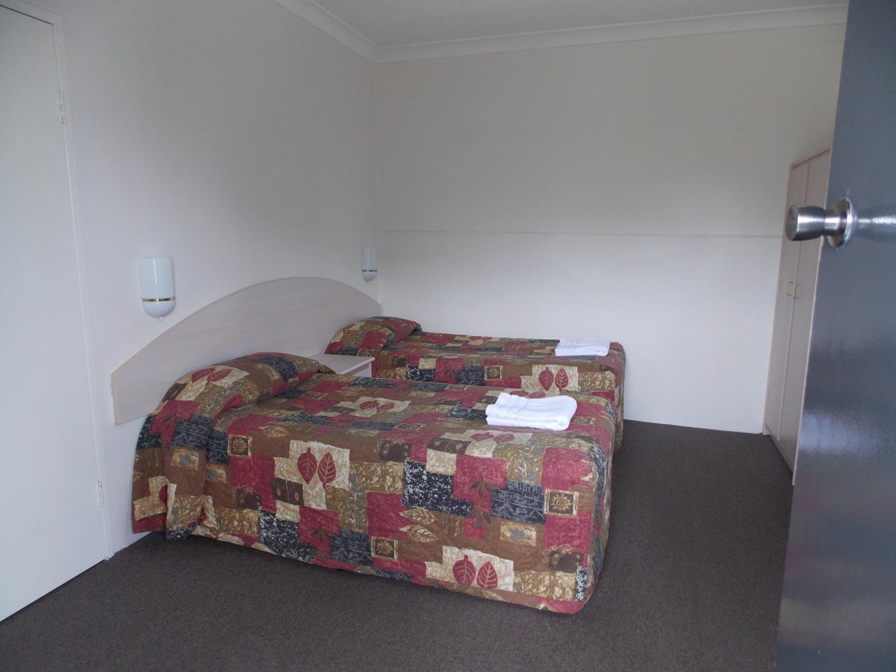 Una cama individual con colcha acolchada en una habitación de paredes blancas y una puerta a la derecha.