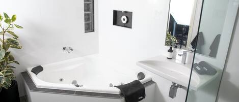 Un baño moderno con una bañera en esquina, cabina de ducha con vidrio y un espejo grande.