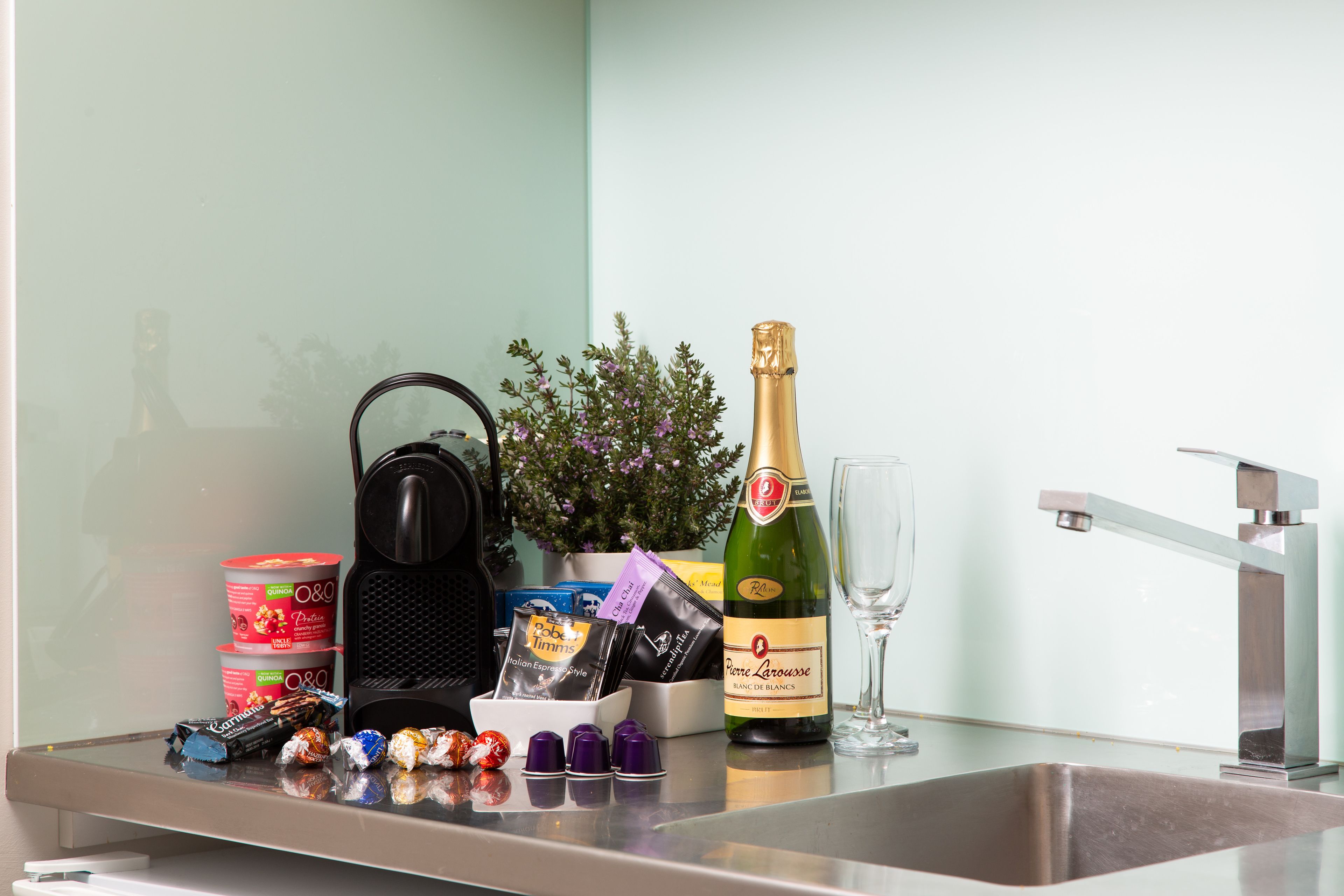 A kitchen counter with a bottle of champagne, a coffee maker, a glass, and various food items.