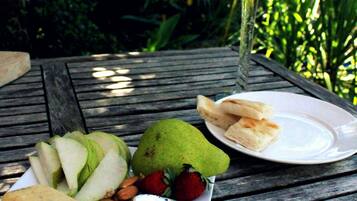 Comida sobre una mesa de madera al aire libre, con una bebida en un vaso, frutas y queso.