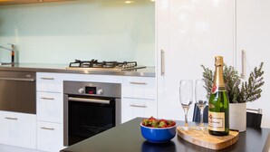 Una cocina moderna con armarios blancos, electrodomésticos de acero inoxidable, una estufa a gas y un bol de fresas sobre la encimera.