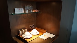 A compact room with a wooden wall, a glass shelf with cups and a sign, a tray with cups and a menu, and a power outlet. - Valentine On George (Haymarket)