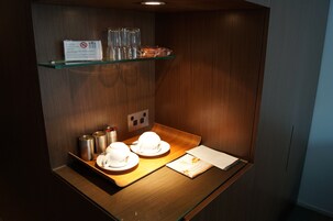Quarto compacto com parede de madeira, uma prateleira de vidro com xícaras e um letreiro, um tabuleiro com xícaras e um menu, e uma tomada.