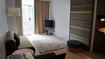 Une chambre d’hôtel comprenant un lit, une télévision, un bureau avec une chaise, une petite table, un canapé, une fenêtre avec des rideaux et un mur décoratif.