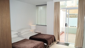A hotel room with two beds, a window with blinds, a door with a handle, and a view of a building labeled "FOREST". - Valentine On George (Haymarket)