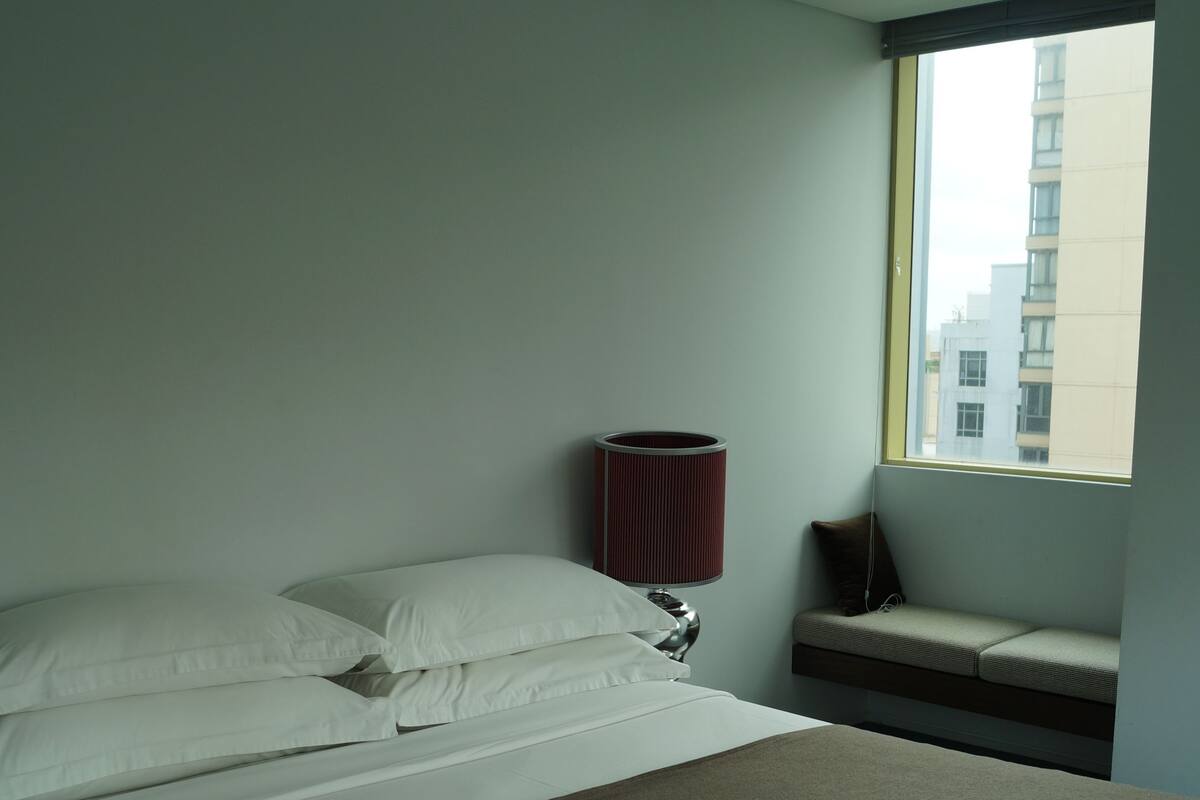 A hotel room with a bed, a window, and a bench by the window.