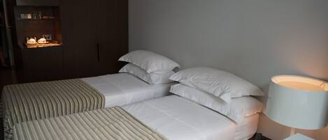 A double bed with a striped blanket, a bedside table, a lamp, and a wardrobe with a shelf.