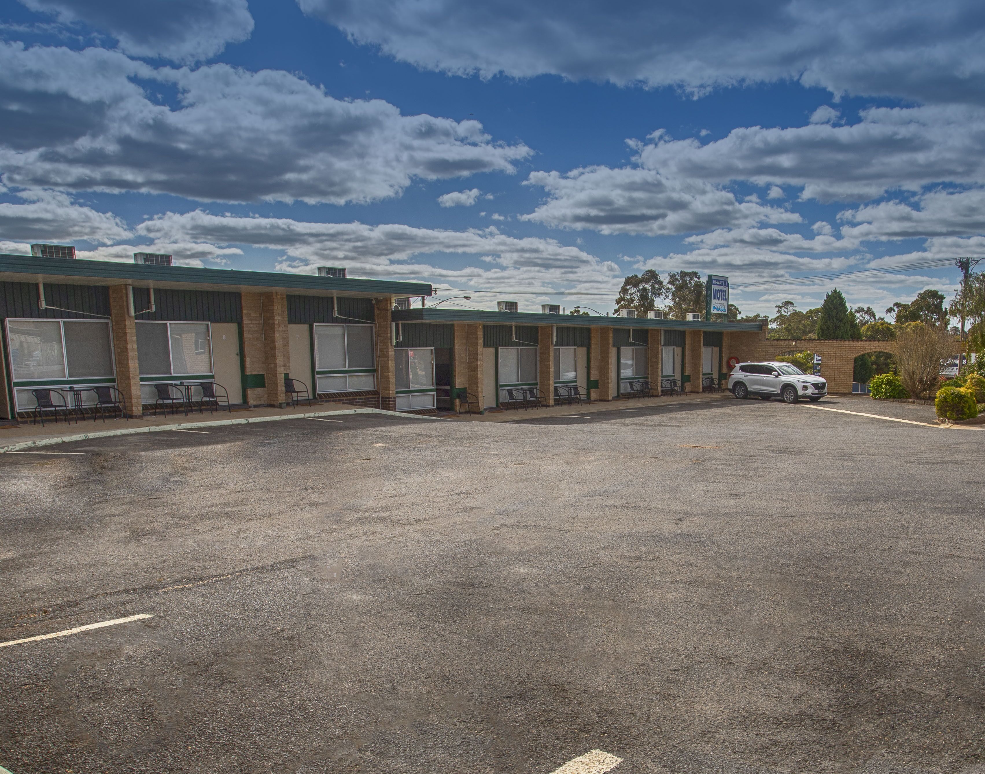 Un motel con una fila de habitaciones, un estacionamiento y un coche blanco estacionado al frente.