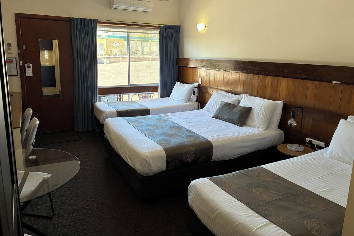 A hotel room with two beds, a desk, and a window with curtains.