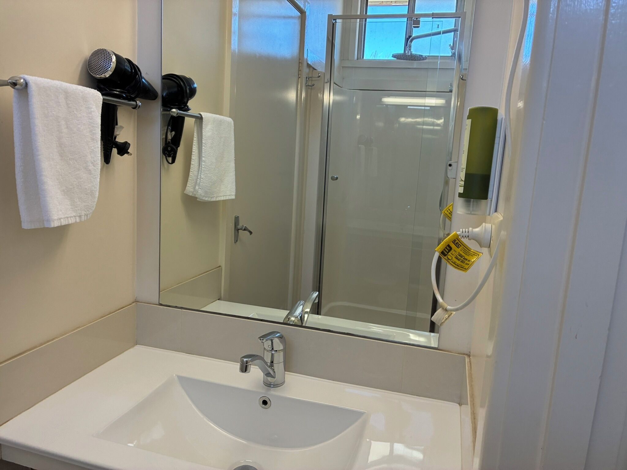 Un baño con lavamanos blanco, espejo y ducha.