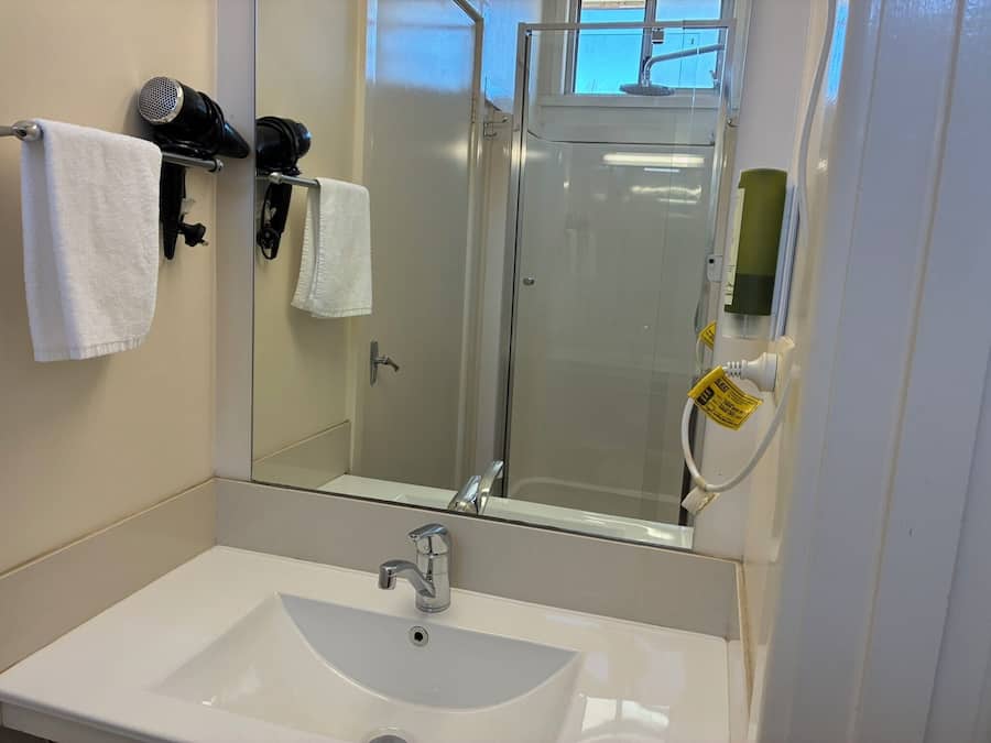 Un baño con lavamanos blanco, espejo y ducha.