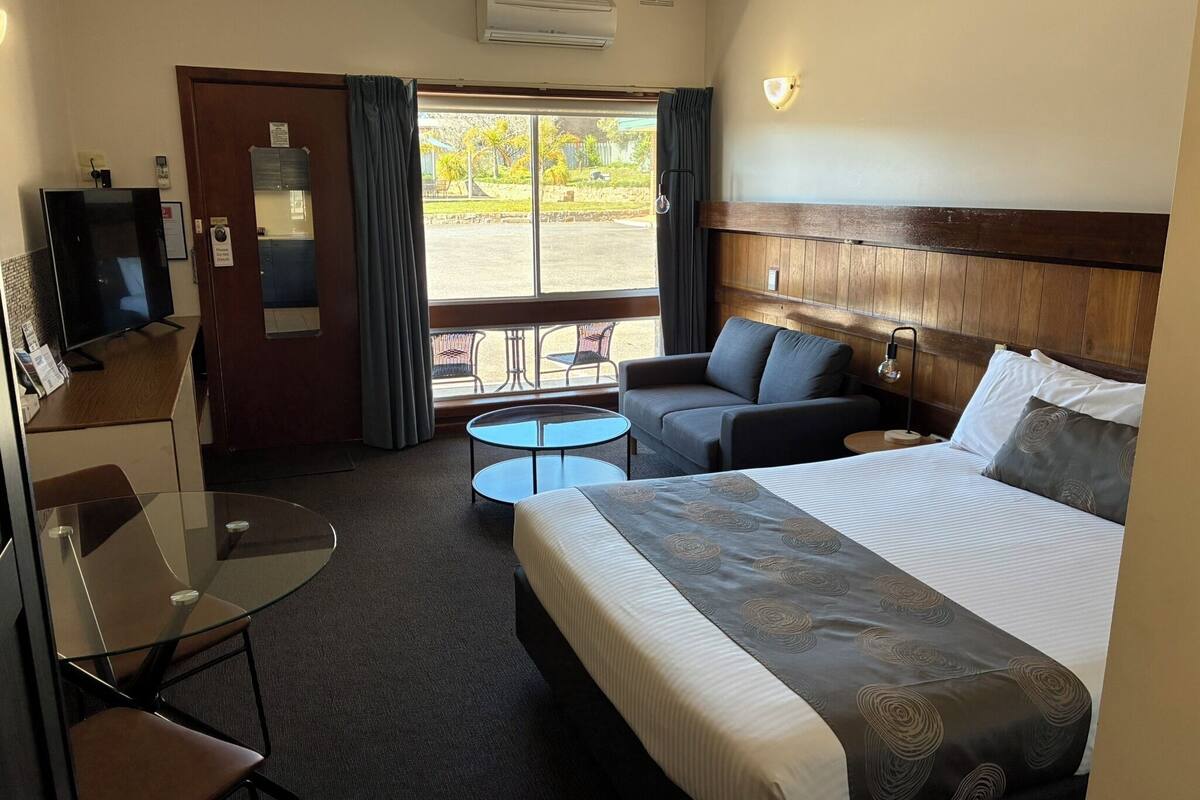 A hotel room with a bed, a sofa, a small table, a TV, and a balcony with curtains.