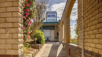 Welcome to our motel, featuring a charming brick facade and a beautiful entrance with a pathway lined with greenery and arches.