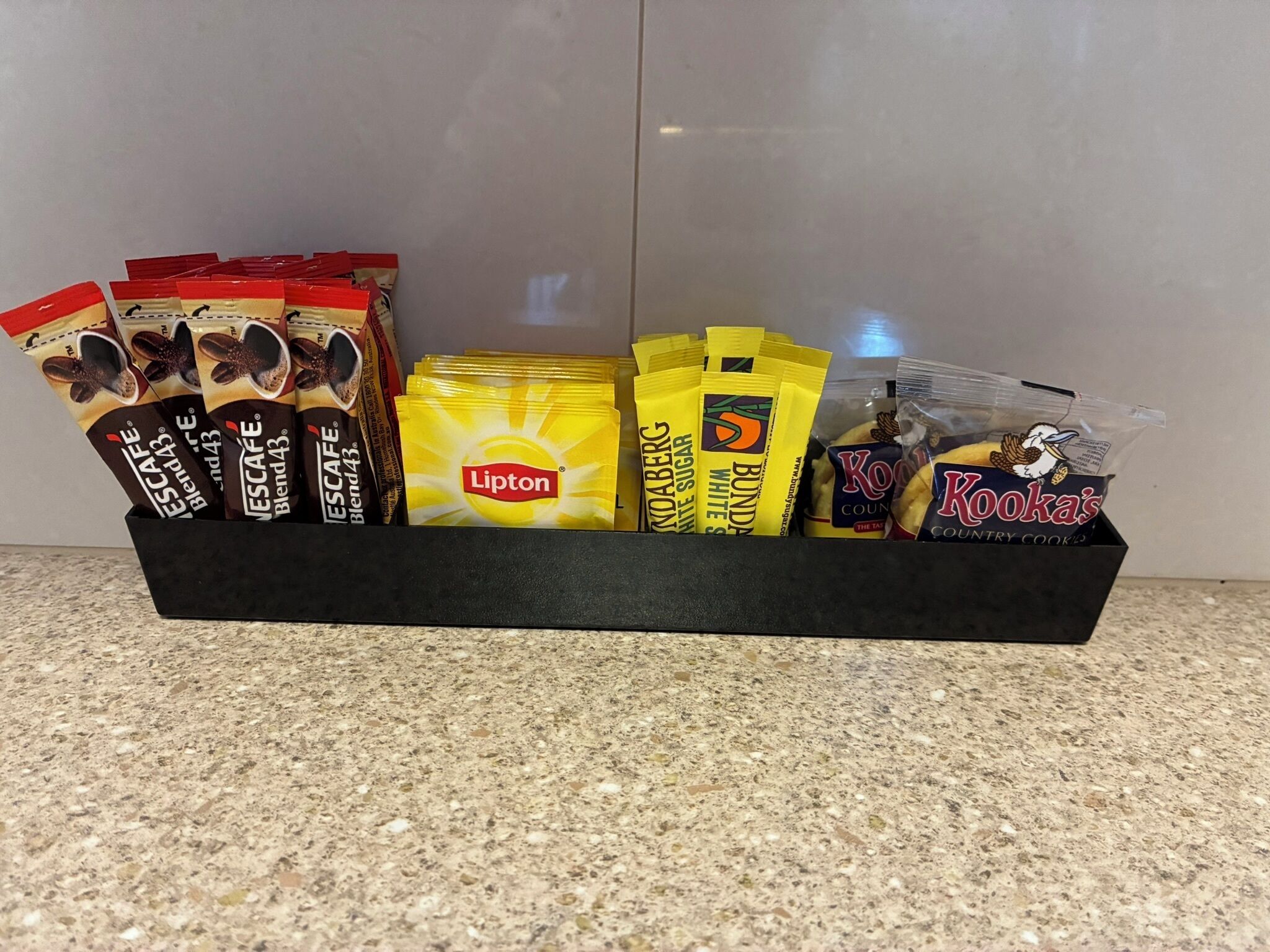 Een dienblad met diverse snacks, waaronder Lipton theezakjes, Kooka's koekjes en Nescafe Blend koffie.
