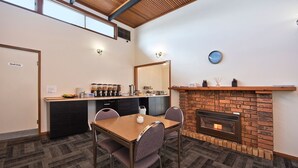 A dining area with a brick fireplace, a kitchen counter with coffee dispensers, and a clock on the wall. - Hi Way Eight Motor Inn (Stawell)