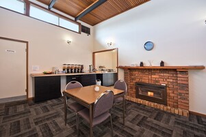A dining area with a brick fireplace, a kitchen counter with coffee dispensers, and a clock on the wall.