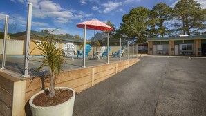 An outdoor seating area with a red umbrella, a potted plant, and a building in the background. - Hi Way Eight Motor Inn (Stawell)