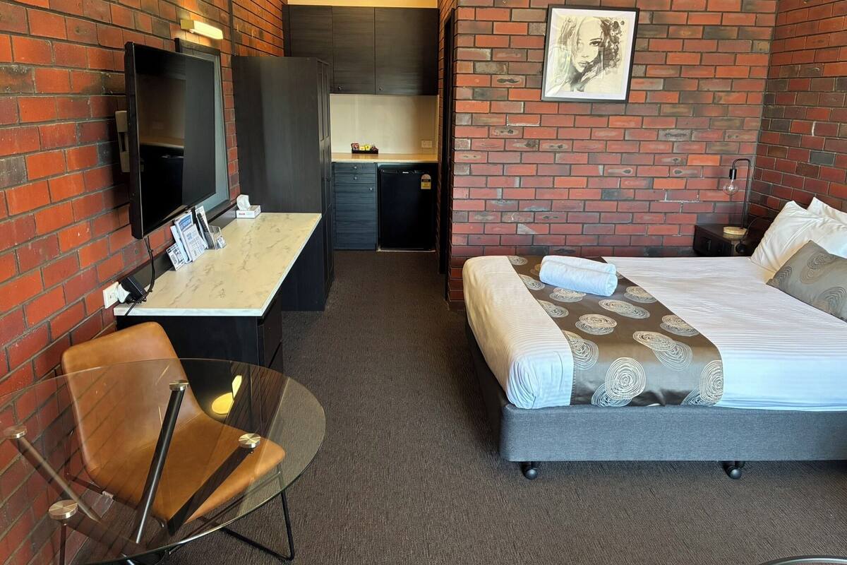 A hotel room with a bed, a desk, a chair, a TV, and a picture on the wall.
