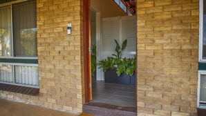 A brick building entrance with a wooden door, a doormat, and a potted plant. - Hi Way Eight Motor Inn (Stawell)