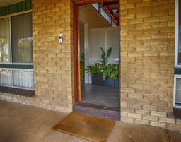 A brick building entrance with a wooden door, a doormat, and a potted plant.