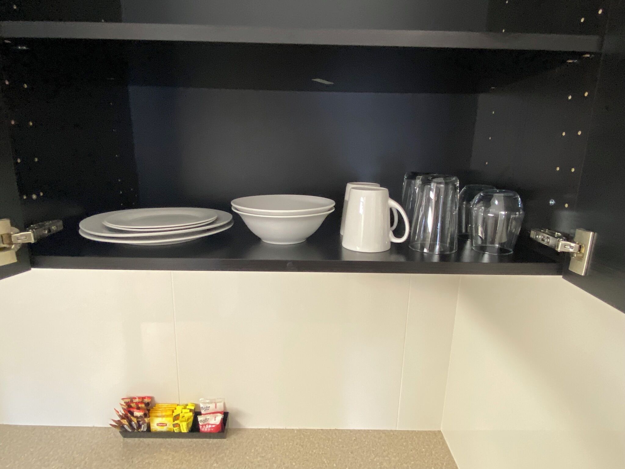 A kitchen counter with white plates, bowls, a mug, and glassware.
