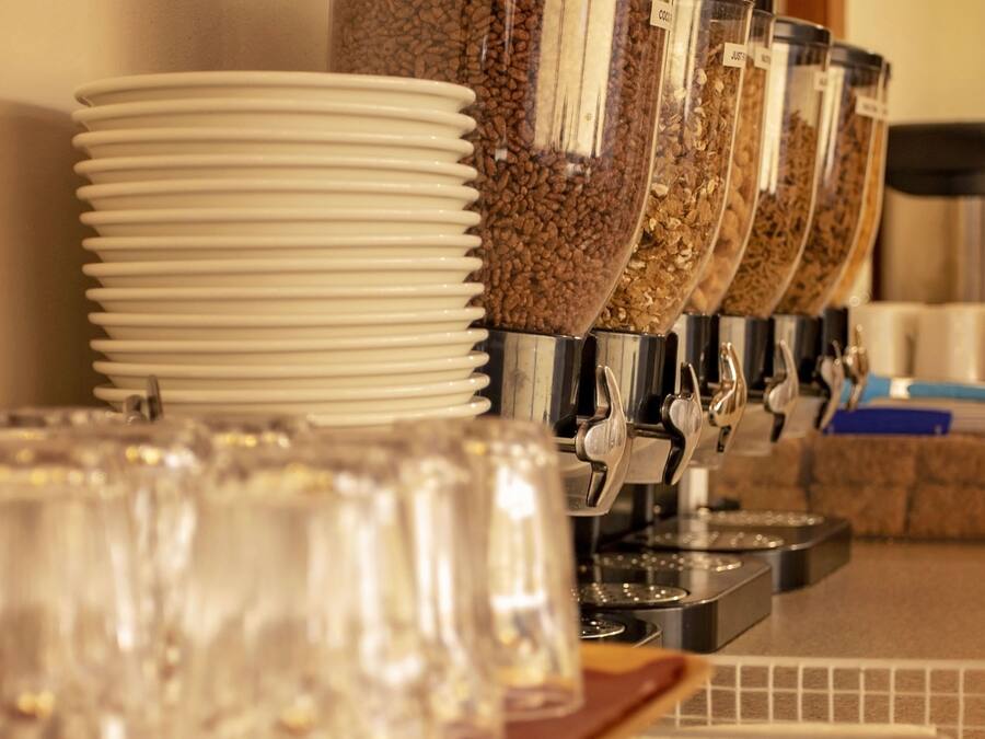 A coffee station with multiple dispensers filled with coffee beans and grounds, surrounded by stacked white plates and clear glasses.