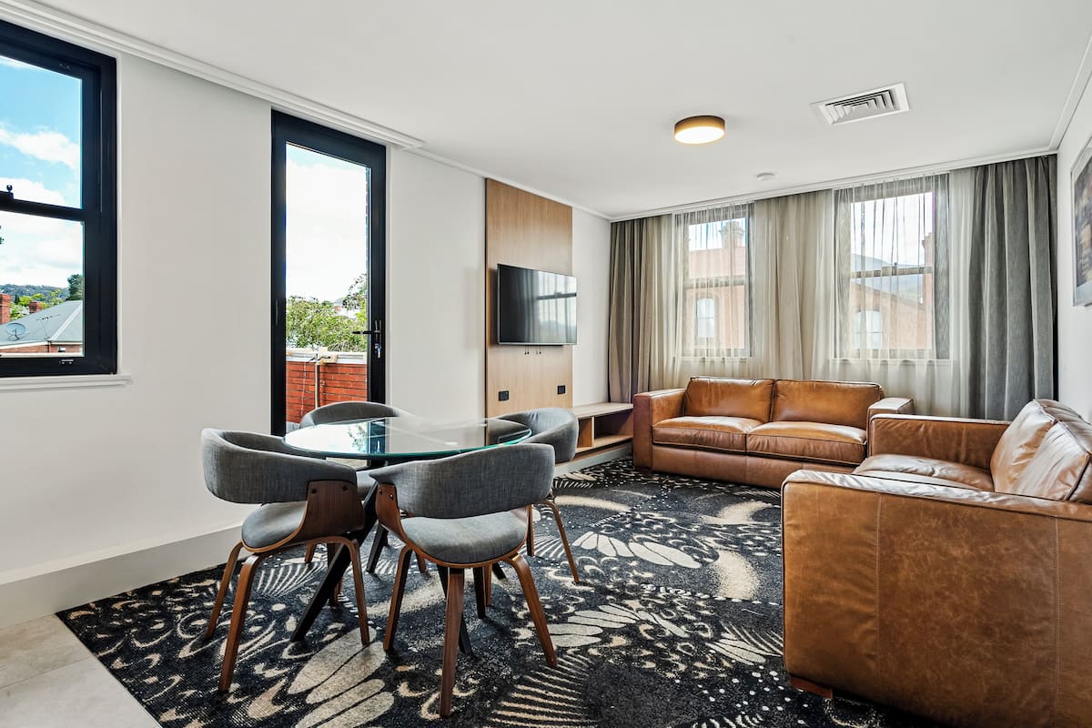 A modern living room with a glass table, leather sofa, and a flat-screen TV.