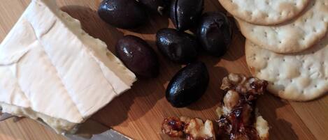 A wooden board with cheese, olives, crackers, and a knife.