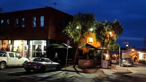 Una escena callejera nocturna con un edificio que tiene un letrero que dice “Prince”. Hay coches estacionados en la calle, y se ve un árbol en primer plano.