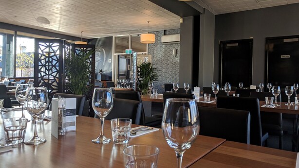 Un restaurante con mesas de madera dispuestas para comer, cubertería de vidrio transparente y una decoración de estilo moderno.