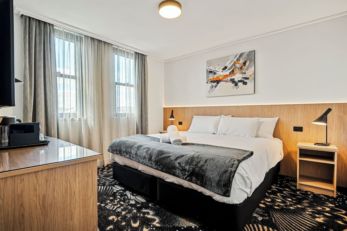 A hotel room with a bed, bedside table, lamp, and artwork on the wall.