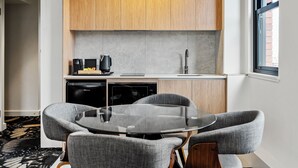 Una cocina moderna con armarios de madera, una cafetera negra, un lavavajillas y una mesa redonda de vidrio con sillas tapizadas en gris.