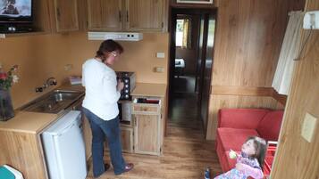 A compact kitchen with wooden cabinets, a refrigerator, and a stove. A child is sitting on a red couch in the living area.