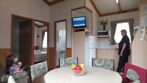 A room with a bed, a television, a microwave, and a dining area with a table and chairs. - Warrnambool Motel and Holiday Park (Warrnambool)