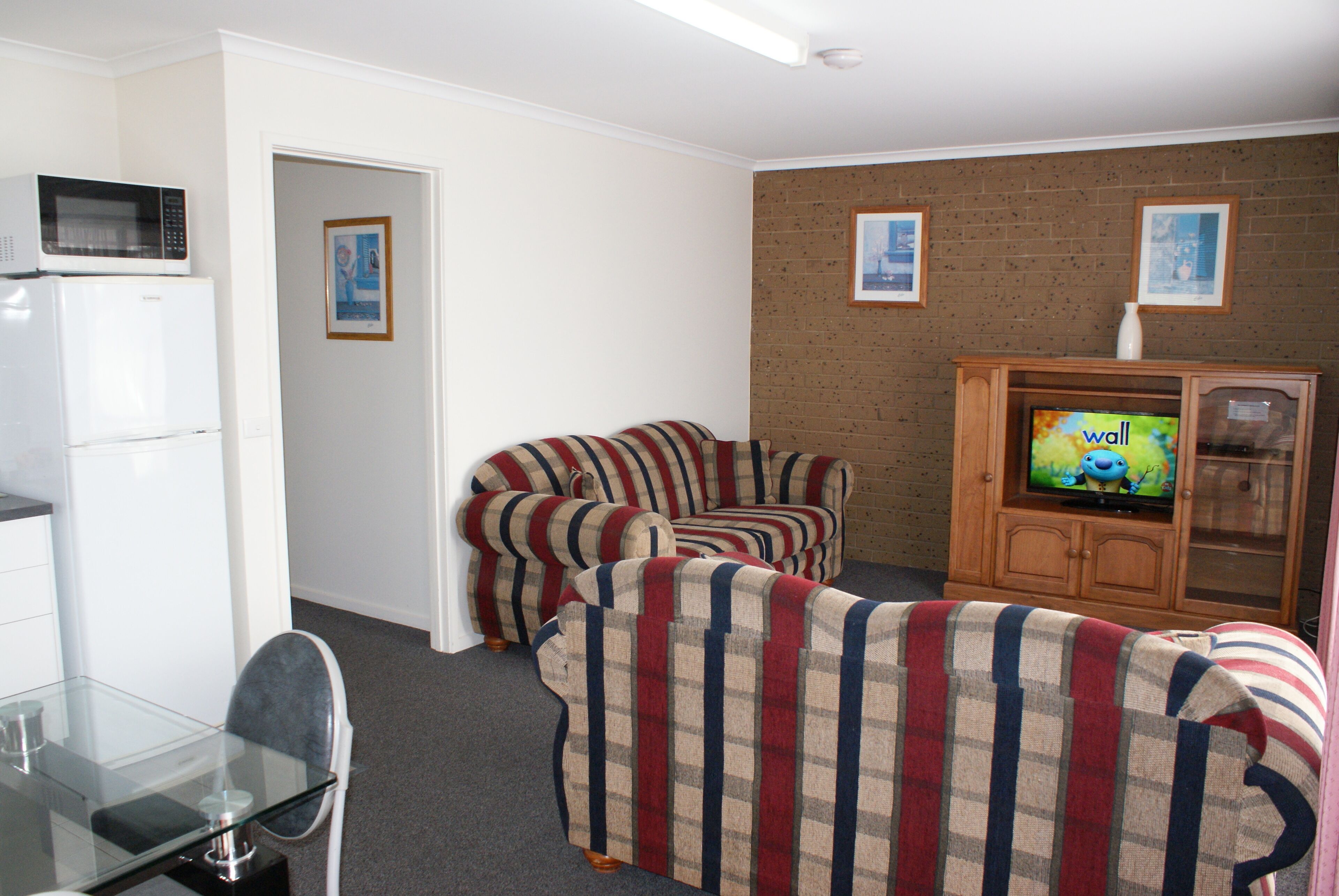 A living room with striped sofas, a glass table, a microwave, and a television on a wooden cabinet.