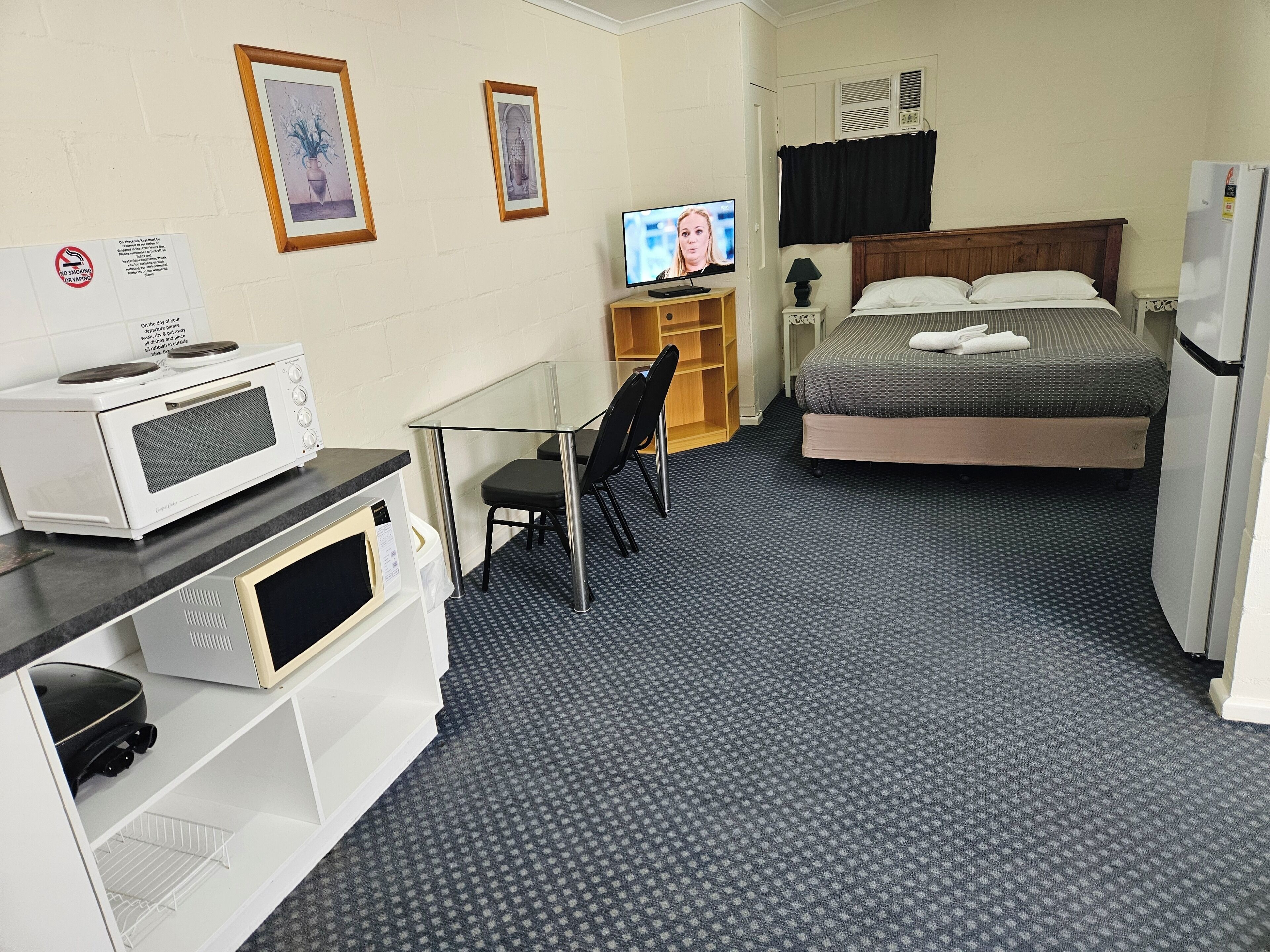 Une chambre d’hôtel de taille réduite, équipée d’un lit, d’une télévision, d’un four à micro-ondes, d’un petit bureau et d’une chaise.