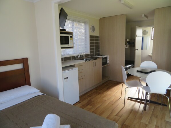 A compact hotel room with a kitchenette, a bed, a dining area, and a bathroom. - Warrnambool Motel and Holiday Park (Warrnambool)
