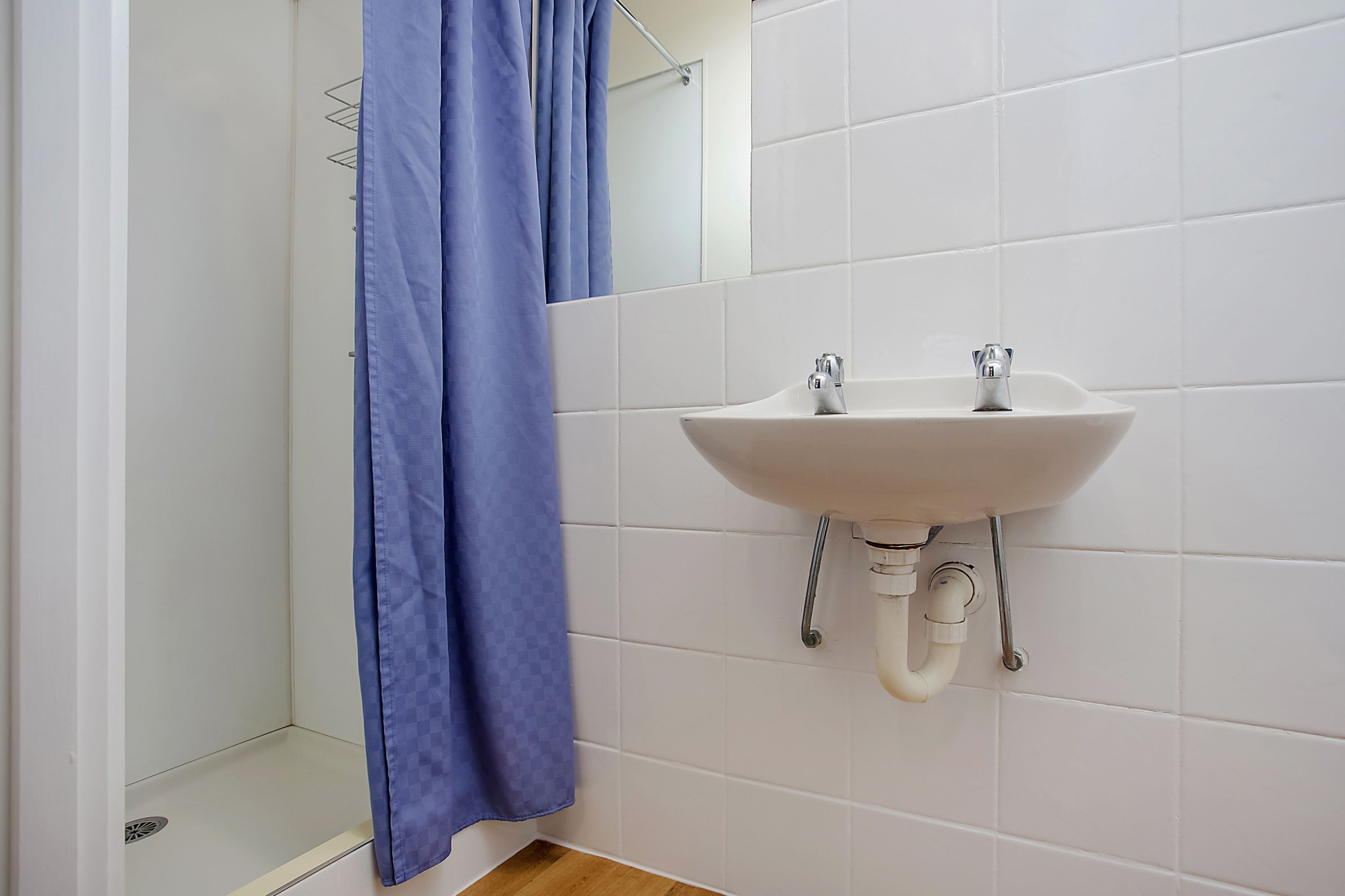 A bathroom with a white sink, a blue shower curtain, and white tiled walls.