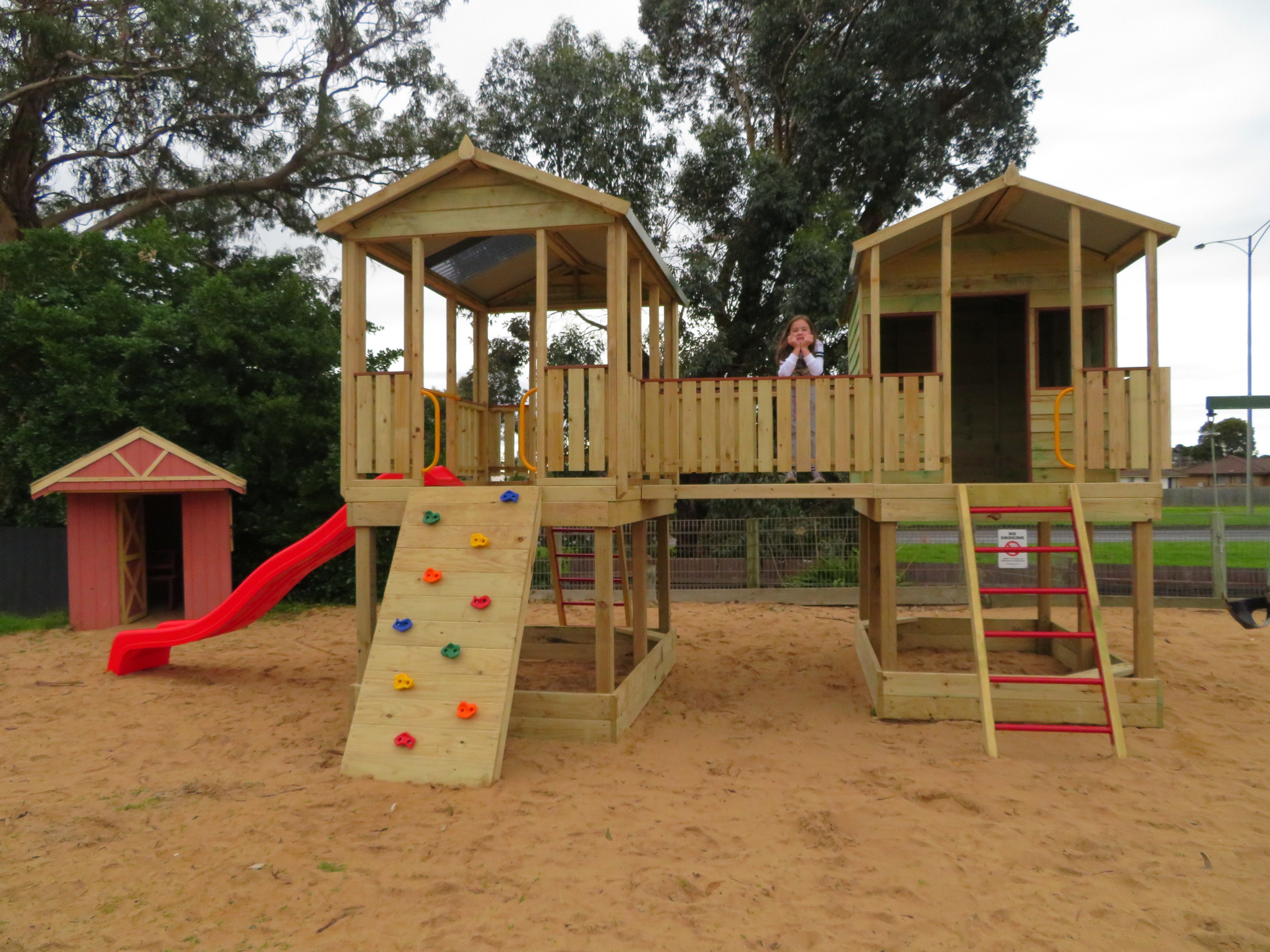 Une structure de jeu en bois, dotée d’un toboggan et d’un mur d’escalade, entourée de sable.