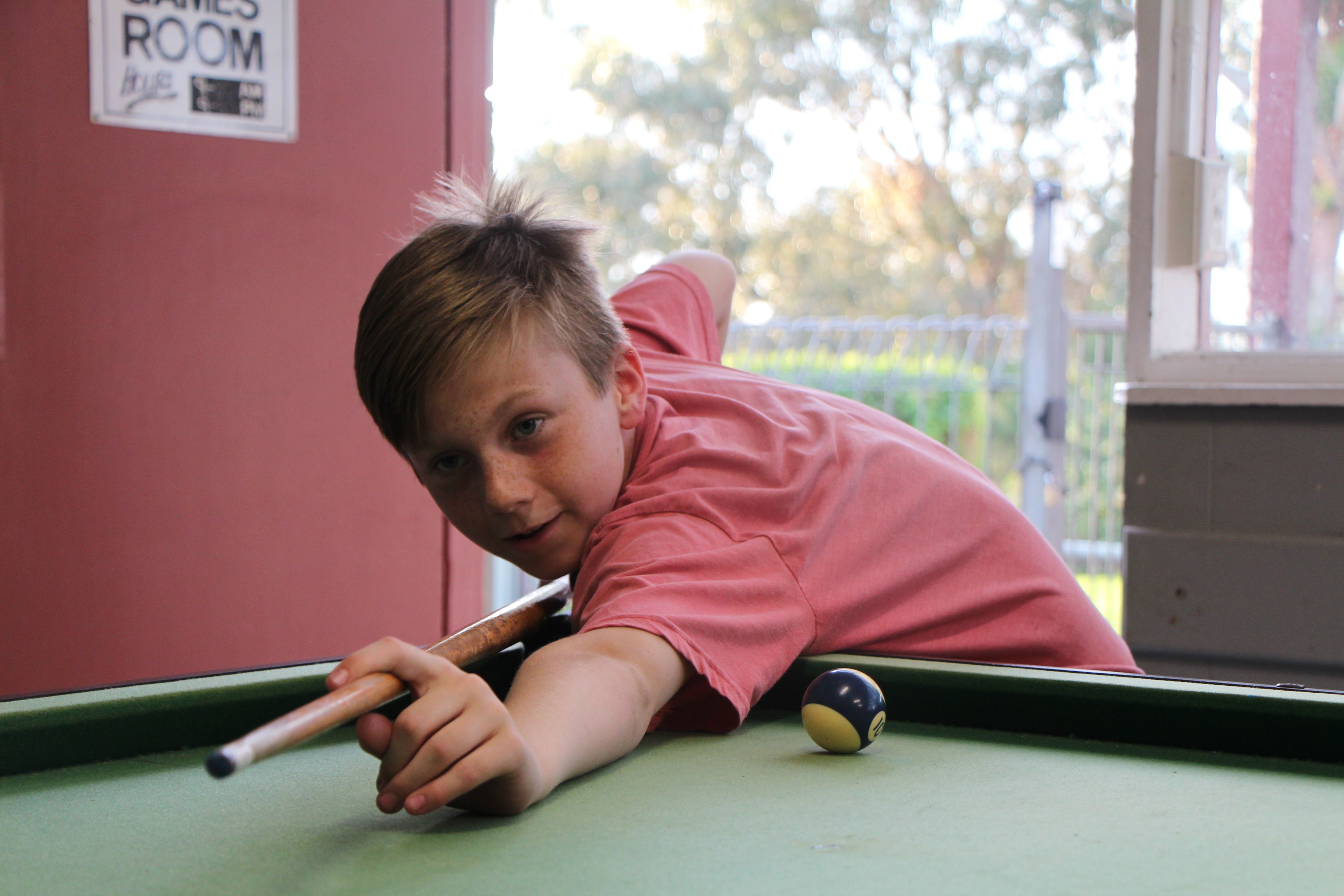 A child leaning over a pool table in a room with a sign that reads "James Room."