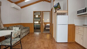 A compact room with a kitchenette, a dining area with a table and chairs, a sofa, and a bed in the background. - Warrnambool Motel and Holiday Park (Warrnambool)