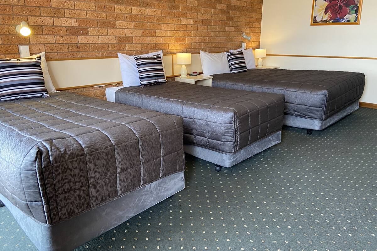 A hotel room with three beds, a brick wall, and a floral painting.