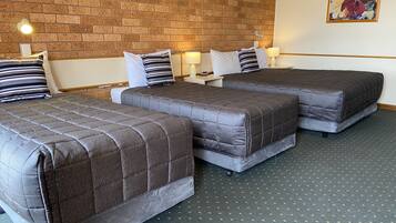 A hotel room with three beds, a brick wall, and a floral painting.